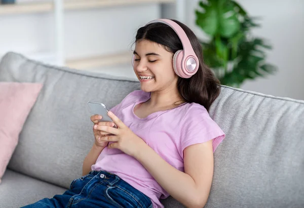 Heureuse adolescente indienne portant un casque, utilisant un téléphone mobile, écoutant de la musique ou un livre audio, communiquant en ligne — Photo