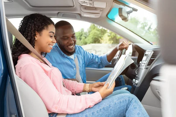 Счастливая черная пара смотрит на бумажную карту, сидя в машине — стоковое фото