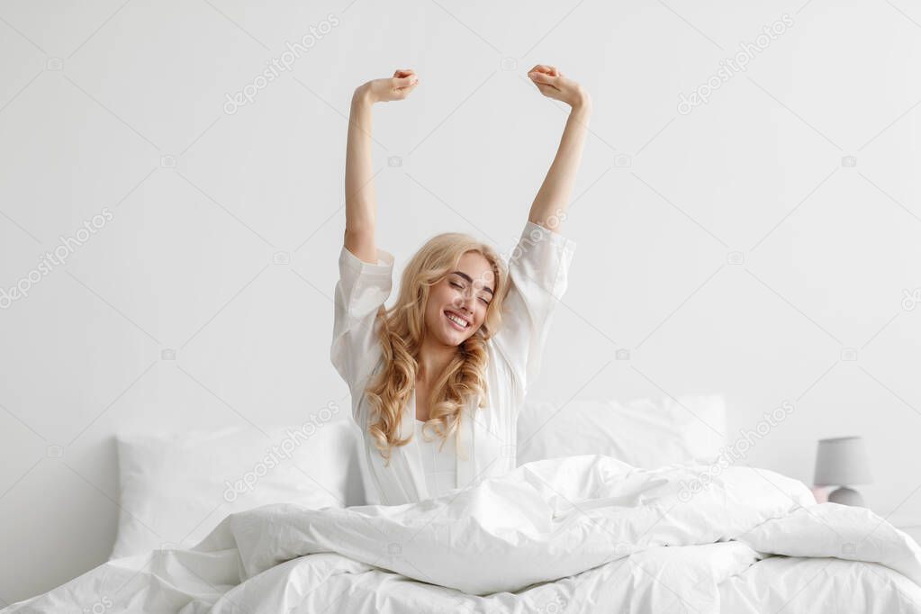 Good morning, smiling young lady waking up fully rested on white bedding, relax at home at weekend, vacation