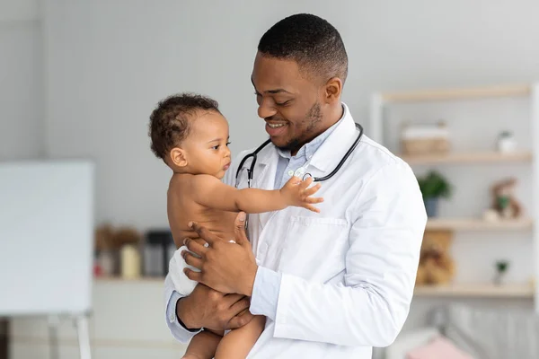 Porträt eines jungen schwarzen Kinderarztes, der einen entzückenden kleinen Jungen in den Händen hält — Stockfoto