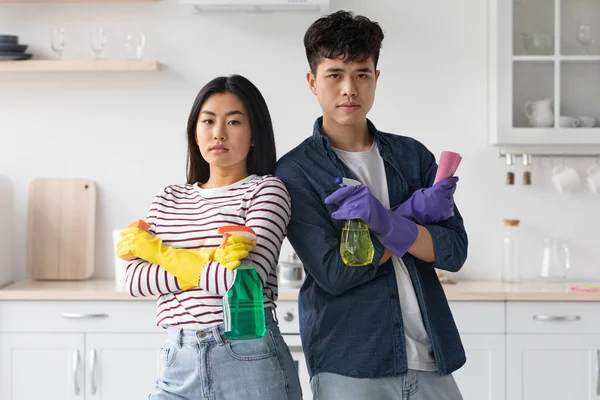 Ernstige aziatische man en vrouw met schoonmaken sprays en sponzen — Stockfoto