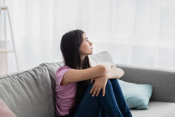 Teen depression. Stressed Indian teenage girl sitting on couch at home, feeling upset and lonely during covid lockdown — Stock Photo, Image