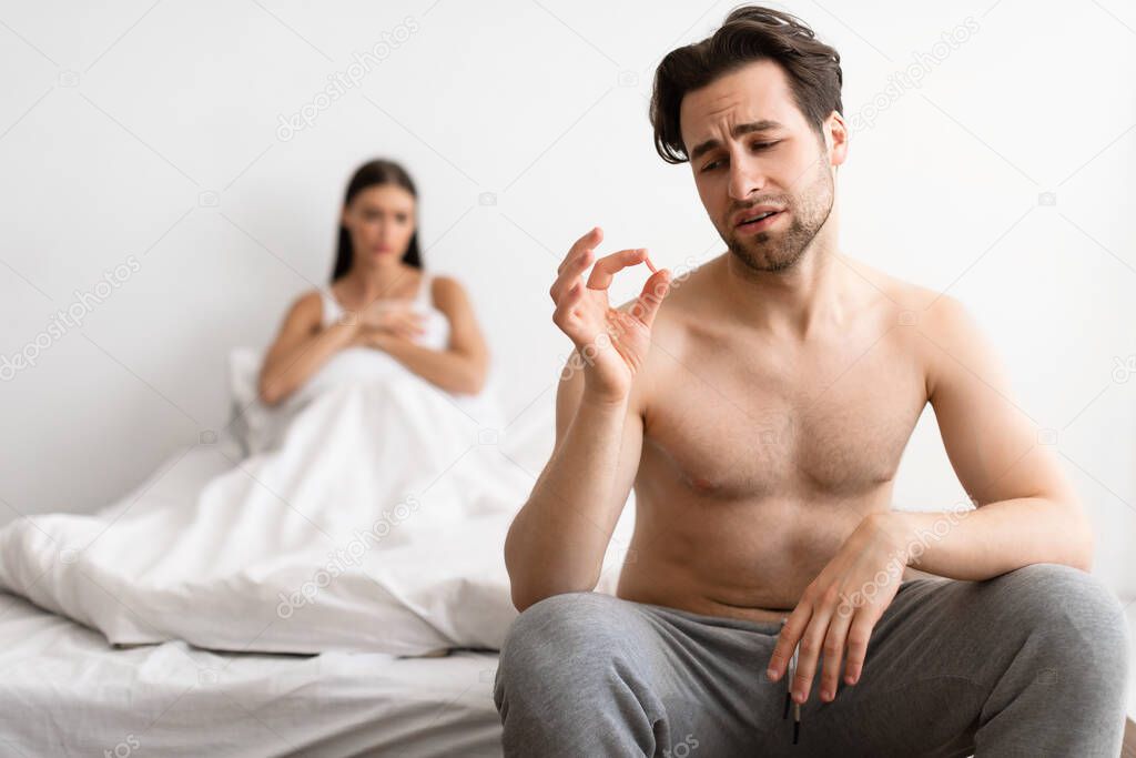 Man Holding Potency Pill While Girlfriend Waiting For Sex Indoor