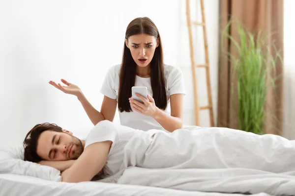 Девушка, держащая изменяющего бойфренда, читает его сообщения в спальне — стоковое фото