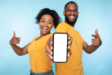 Neşeli siyah çift ekranda akıllı telefonu gösteriyor, mobil uygulama öneriyorlar, web sitenizi tanıtıyorlar.