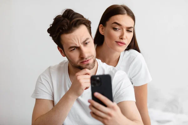 Novia celosa espiando a novios Teléfono celular leyendo mensajes en el dormitorio —  Fotos de Stock