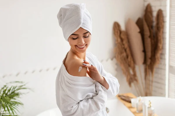 Mulher feliz aplicando hidratante loção cuidando do corpo no banheiro — Fotografia de Stock