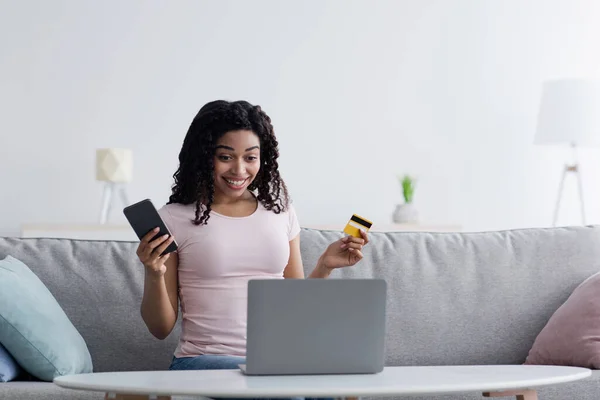 Oturma odasında dinlenirken kredi kartıyla online alışveriş yapan akıllı telefon kullanan genç bir kadın. — Stok fotoğraf