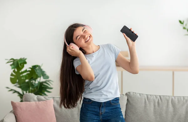 Felice ragazza adolescente indiana con cuffie e dispositivo mobile che balla sulla musica a casa — Foto Stock