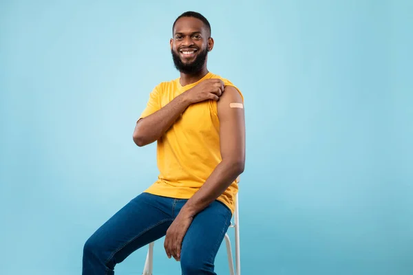 Vacuna Covid-19. Joven negro que muestra vendaje adhesivo en el hombro después de la vacunación contra el coronavirus, fondo azul —  Fotos de Stock