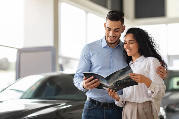 Beautiful middle-eastern couple checking booklet in car salon — Stock Photo, Image