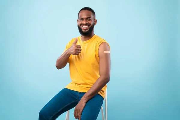 Vacinação com Covid-19. Homem negro sorrindo mostrando braço com ajuda banda após tiro de vacina coronavírus, mostrando o polegar para cima — Fotografia de Stock