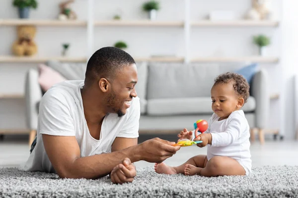 Atividades de desenvolvimento com bebês. Pai negro brincando com criança infantil em casa — Fotografia de Stock