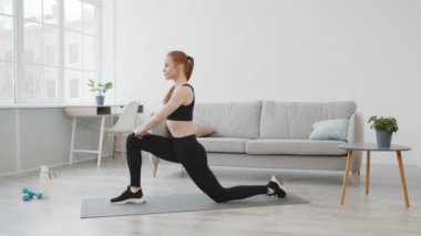 Spor salonundaki kadın bacaklarını esnetiyor. Evinde ileri doğru hamle yapıyor.