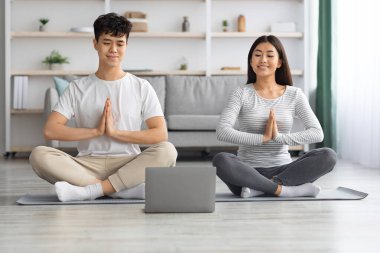 Rahat Asyalı aile evde sabah meditasyonu yapıyor, dizüstü bilgisayar kullanıyor.