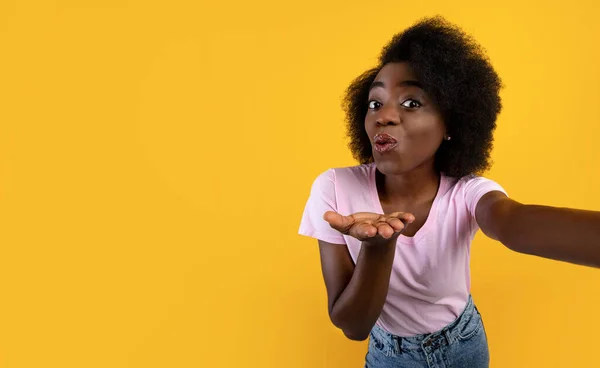 Joyful Africano americano senhora tomando selfie, soprando beijo de ar para câmera sobre amarelo estúdio fundo, espaço livre — Fotografia de Stock