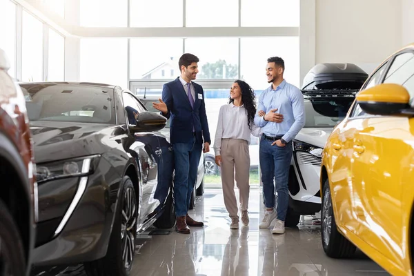 Arab guy sales assistant giding young family by car salon — Stock Photo, Image