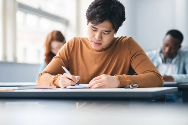 Ázsiai férfi diák ül íróasztal az osztályteremben írás vizsga — Stock Fotó