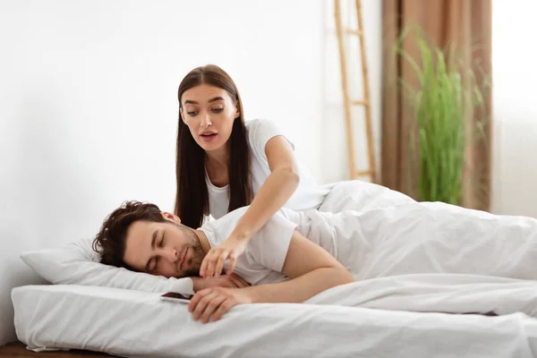 Jaloerse vrouw neemt echtgenoten telefoon terwijl hij slaapt in de slaapkamer — Stockfoto