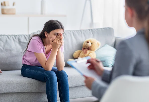Depressed Indian teen girl having consultation with psychologist at office, covering face, talking about problems — Stock Photo, Image