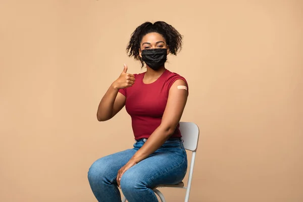 Vrolijke zwarte dame met gevaccineerde arm met pleister na covid-19 vaccininjectie, duim omhoog gebaren — Stockfoto