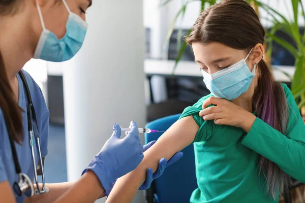 Школярка отримує ін'єкції вакцини проти коронавірусу сидячи з лікарем в приміщенні — стокове фото
