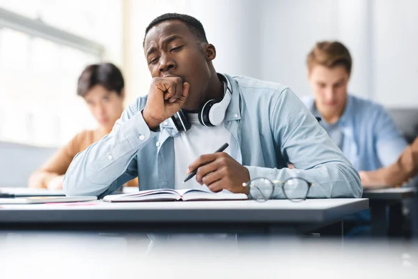 Noir mâle étudiant bâillant assis au bureau en classe — Photo