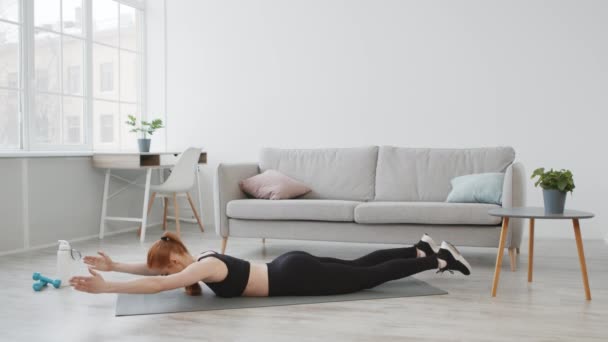 Mujer haciendo ejercicio levantando piernas y brazos acostada en el estómago en interiores — Vídeo de stock