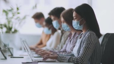 Koruyucu maskeler takan bir grup öğrenci üniversitede ders veriyor ve dizüstü bilgisayarlara notlar yazıyorlar.