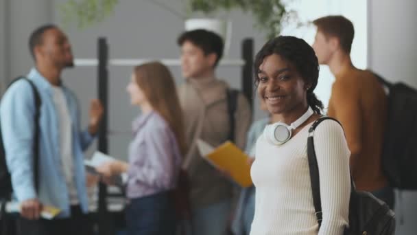 Jovem e alegre estudante afro-americana sorrindo feliz para a câmera, de pé perto de seus diversos colegas de grupo, espaço livre — Vídeo de Stock