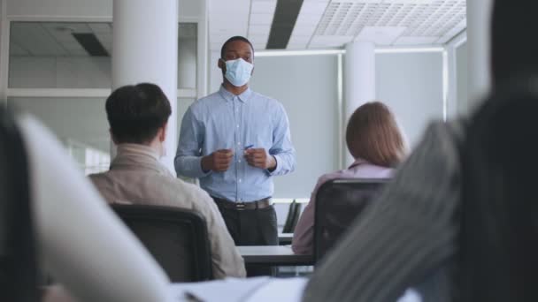 Processus d'éducation. Professeur afro-américain en masque de protection demandant aux élèves de travailler, les élèves levant la main pour obtenir une réponse — Video