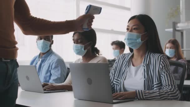 Группа студентов в защитных масках для лица, печатающих на ноутбуках, неузнаваемая температура учителя — стоковое видео