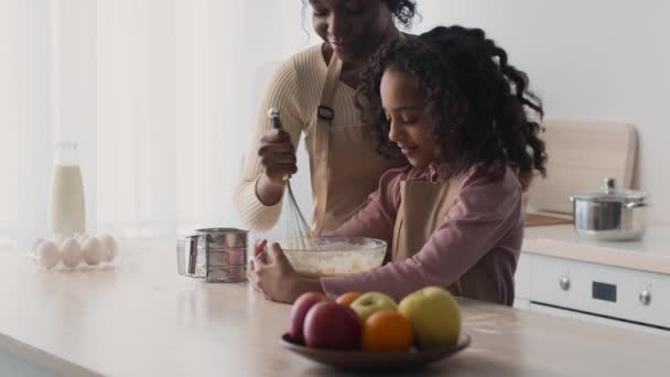 Linda chica afroamericana ayudando a su madre con hornear, mujer mezclando masa en un tazón de vidrio, enseñando a su hija — Vídeos de Stock