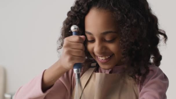 Micuţa casnică. Fată africană americană fericită pregătind aluat dulce și degustare bucată din ea la bucătărie, mișcare lentă — Videoclip de stoc