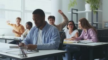 Zorbalık. Afrikalı Amerikalı çocuk notlar yazıyor, bir grup öğrenci ona kağıt top atıyor ve sınıfta gülüyor.