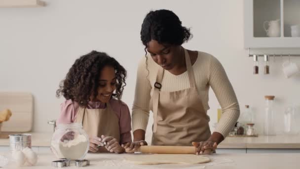 Young african american mother rolling out dough on table, little daughter cutting cookies with metal cutter, slow motion — Stock Video