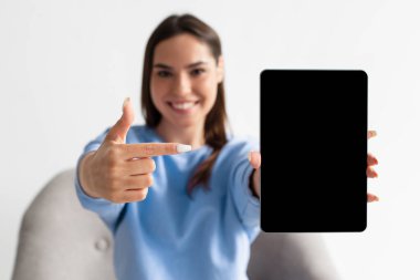 Neşe dolu genç kadın tableti boş ekranla gösteriyor, yeni uygulamayı tanıtıyor, web sitesi için yer sunuyor