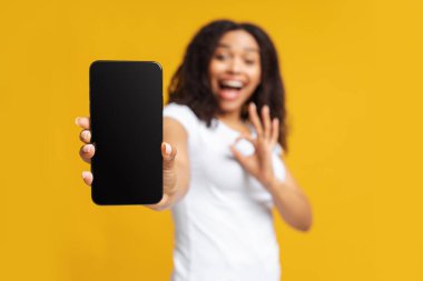 Güzel mobil uygulama. Neşeli siyah kadın, beyaz ekranlı akıllı telefon ve sarı arka planda güzel hareketler gösteriyor.