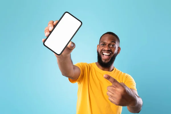 Neue atemberaubende mobile App. Schwarzer Mann zeigt auf Smartphone mit leerem Bildschirm auf blauem Hintergrund, Attrappe — Stockfoto
