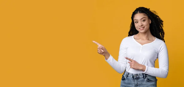 Glimlachende Millennial Afro-Amerikaanse vrouw wijzen op kopieerruimte op gele achtergrond — Stockfoto