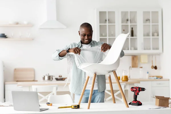 Feliz hombre negro recibir nuevos muebles y empezar a desempacar silla en la mesa en el interior de la cocina, espacio de copia — Foto de Stock