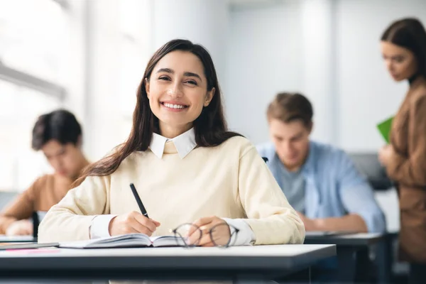 Estudante sorridente sentada na mesa escrevendo em seu caderno — Fotografia de Stock