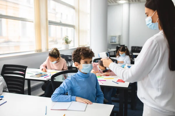 Profesor con termómetro sin contacto que mide la temperatura del niño pequeño —  Fotos de Stock