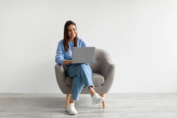 Heureuse dame caucasienne assise dans un fauteuil avec ordinateur portable moderne, étudier à distance ou avoir une réunion d'affaires — Photo