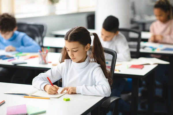 Portret van een klein meisje dat achter een bureau zit te schrijven of tekenen — Stockfoto