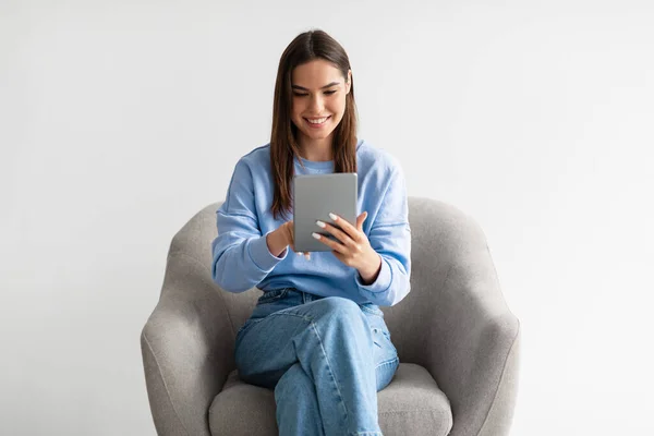 디지털 태블릿을 사용하는 젊은 캅카스 여성, 인터넷이나 소셜 미디어를 둘러보고 하얀 배경에 안락 의자에 앉아 — 스톡 사진