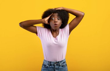 Hadi canım. Çok şaşırmış siyah bir kadının portresi kameraya bakıyor ve sarı arka planda dikilip başını tutuyor.