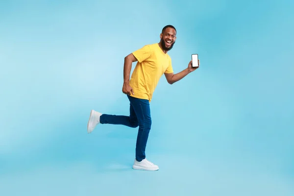 Junger Afro-Typ mit leerem Smartphone, das auf blauem Hintergrund läuft, demonstriert Mockup für mobile App, Website — Stockfoto