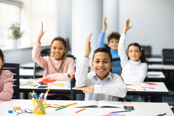 Happy little school children raising hands at classroom