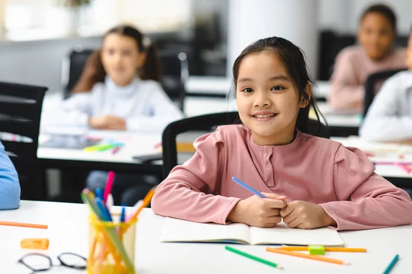 Retrato de chica asiática pequeña sentada en el escritorio en el aula —  Fotos de Stock